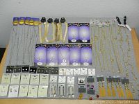 Top-down photo of a large assortment of new old stock jewelry laid out in rows on a table, showing gold-tone and silver-tone necklaces, earrings, pendants, and jewelry components on various backing cards.
