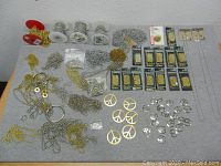 Photo of the full lot spread out on a gray surface showing bead chains in silver and gold tones, peace sign pendants in silver and gold finishes, some loose some packaged.
