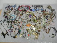Top view showing large assortment of colorful costume necklaces and bracelets in tangled arrangement on gray background.