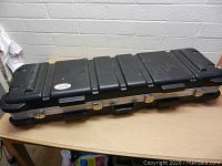 Black hard plastic rifle case closed on table with visible handle, latches and ridged design.