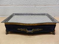 Front view of the vanity tray showing the mirrored top, silverplated frame and blue velvet drawer with metal handle and feet.