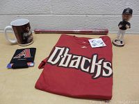 Full lot showing red D-backs shirt, mini bat, koozie, mug, and Randy Johnson bobblehead figurine