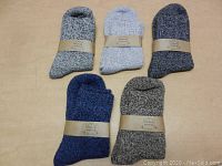 Top-down view of five pairs of wool socks arranged flat in a rectangular formation, showing colors, knit texture and packaging bands intact.