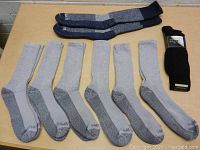 Six pairs of Dickies light gray socks with dark gray reinforced toes and heels laid out flat accompanied by one pair of dark gray and navy Carhartt wool socks, and three black Gold Toe socks in original packaging.