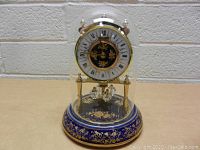 Front view of mantle clock inside a clear glass dome showing Roman numerals, gold accents, and floral motifs.