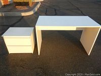 White desk and 2 drawer cabinet shown side by side on outdoor pavement, a clean and minimalist style in white color.