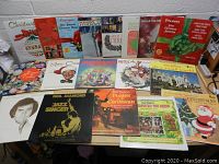 Photo showing multiple vintage Christmas vinyl records laid out on table including albums by Chipmunks, Neil Diamond, Kenny Rogers & Dolly Parton, Firestone holiday gift albums, Disney's Pirates of the Caribbean, among others.