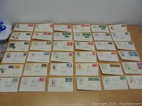 Wide shot of large collection of about 36 First Day of Issue stamped envelopes from the 1940s with varied stamps and cachets spread on a table.