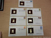 Seven commemorative envelopes each with a distinct gold replica stamp and postmark, displayed legally flat on a surface