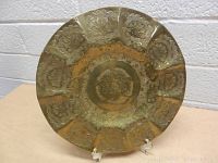 Front view of the brass plate showing floral and geometric engravings with scalloped edges and patina.