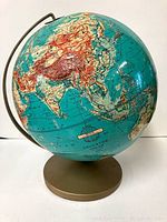 Front view of the vintage globe showing Asia, mounted on a gold-tone stand with visible wear.