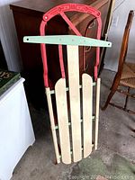 Front view of the vintage sled showing the three wooden slats, red metal handle and pale green crossbar.
