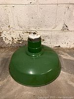 Photo showing vintage light fixture base and dome painted green, placed on the ground next to a stone wall.