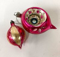 Two vintage Christmas ball ornaments laying flat showing their shapes and decorative details.