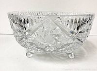 Full side view of a clear crystal footed bowl showing geometric cut patterns and three small rounded feet.