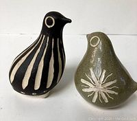 Pair of two vintage mid century modern pottery bird figurines, one black with beige stripes and one olive green with a white floral design, photographed on white background.