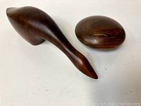 Two rosewood sculptures shown side by side - a stylized bird and an oval carving.