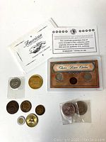 Lot of 12 coins including a three-coin set with certificate, two individual coins in protective sleeves, multiple loose coins, and a token. White envelope labeled American Coin Treasures included.