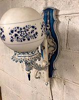 Close-up of vintage blue and white wall sconce mounted on wall showing spherical glass shade with floral pattern and ornate blue and white metal fixture.