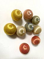 Top down view of 9 glittery textured Christmas ball ornaments in gold, champagne, copper, red, and multi-tone blue sparkle finish with white hanging caps.