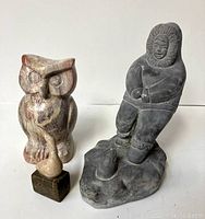 Photo shows stone owl and First Nations figure side by side with good lighting to reveal carved details.