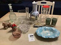 Full lot view showing 16 assorted pieces of glassware and decorative items including decanters, vases, candy dishes, and figurines.