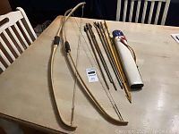 2 vintage wooden recurve bows, 7 arrows with various feathers, and white arrow case on table