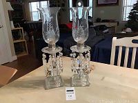 Pair of vintage glass hurricane lamps on table, showing full lamp height and etched glass chimneys