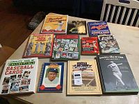 Collection of 11 baseball books arranged on a light-colored table including titles on baseball cards, ballparks, notable games, and Hall of Fame.