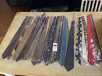 Photo of 36 men's dress ties laid out on a surface, all individually packaged and arranged in rows showing various colors and patterns.