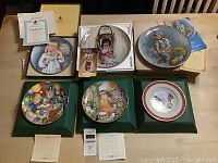 Six collector plates in original boxes along with certificates of authenticity and a small figurine in a box on a wooden table.