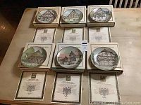 Six German half-timbered house collector plates arranged on a table, each with original box and certificate of authenticity in front, showing condition and authenticity documents.
