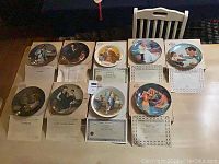 Nine assorted Edwin Knowles collector plates displayed on table with Certificates of Authenticity visible. Plates depict various family, Americana, and island scenes.