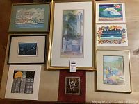 Eight pieces of wall art displayed on a surface. Includes framed and unframed works featuring landscapes, marine life, and architectural subjects.