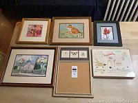 Six framed or boxed artworks arranged on a flat surface showing varied subjects including buildings, animals, flowers, and abstract elements