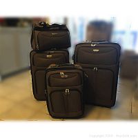 Photo of the full 4-piece nylon luggage set showing three sizes of wheeled roller bags and one small tote bag in dark nylon fabric with exterior pockets.