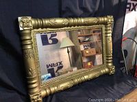 Full view of the antique mirror showing the brass-colored wood frame with carved wheat and flower motifs and reflective glass.