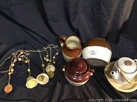 Overview of all earth tone ceramic items including pots, teapot, and bell chimes on dark cloth background.