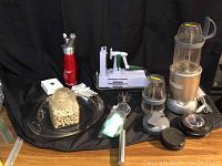 Full lot overview showing Nutri-Bullet blender, cream whipper, spiralizer, Pyrex glass bakeware, jar of pie weights, and pie crust edges.