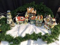 Overview photo showing the five lite-up Christmas houses arranged on a white fabric base with green garland surrounding them.