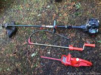 Craftsman weed whacker with long shaft, loop handle, and red propane burner attachment and Homelite electric hedge trimmer laid on forest ground
