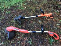 Two electric weed whackers lying on the ground, showing overall length and design.