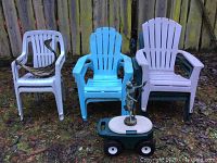 Five plastic Adirondack style chairs and two other plastic chairs with a wooden duck hanging piece on one chair and rolling garden tool box below the sculpture