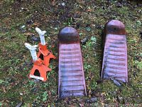 Two orange jack stands and two heavy-duty metal car ramps placed on grass, showing signs of use.