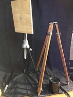 Two tripods side by side, one wood, one metal with wooden platform on top.
