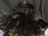 Front view of black fur jacket showing texture of long dark fur on sleeves and body