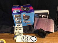 Full lot showing boxed Gold Beam Co-Producer, slide mounts in sleeves, reels, and accessories laid out on black fabric.