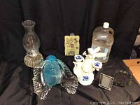 Photo showing all items in the lot: blue glass face with wing-like hair, white plaster angel, two small frames, oil lamp with chimney and bottle of lamp oil.