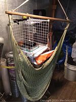 Sage green rope porch swing with a wooden spreader bar hanging indoors in a storage area.