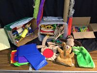 Overview of kid's toys including wooden train set with track, colorful kites, hand puppets, and noisemakers on a table.